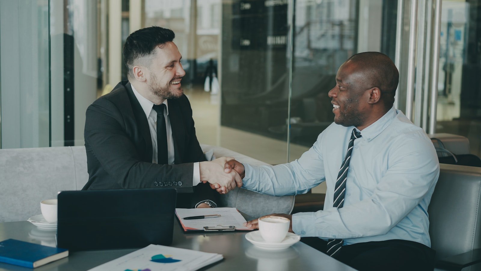 Two business partners shaking hands over deal documents